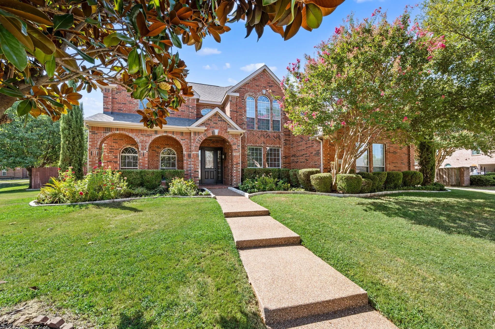 Brick facade residence featuring arched entryways, a stepped concrete walkway, arched windows, and established landscaping
