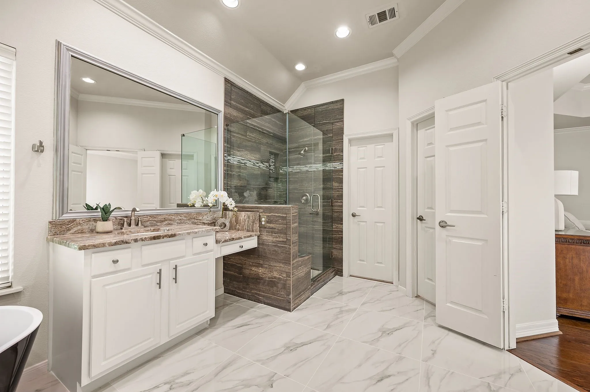 Spacious bathroom featuring a large vanity with stone countertop, walk-in shower with glass enclosure, white cabinetry, and large format marble-look tile flooring