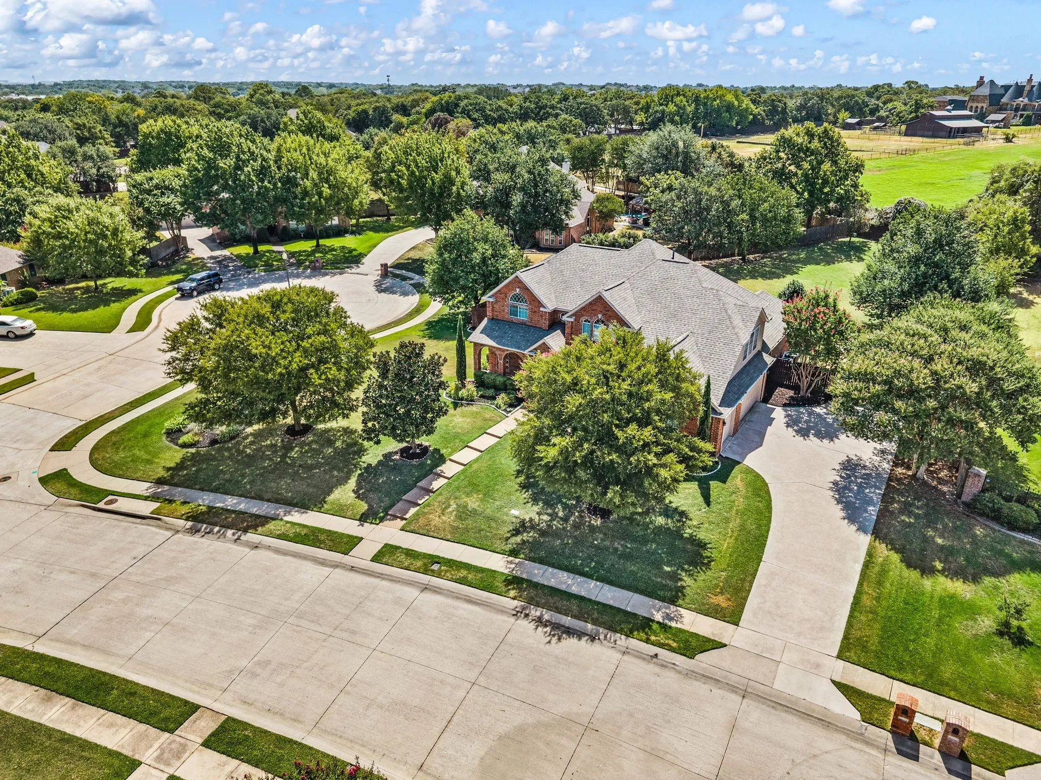 Brick exterior residence with a gray shingle roof, concrete driveway, stone pathway, and mature landscaping