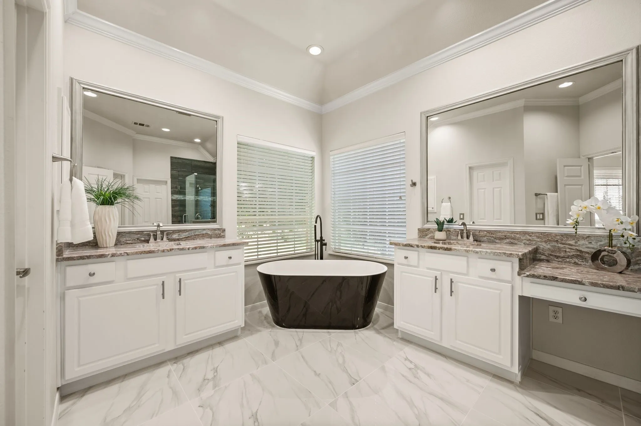 Freestanding soaking tub with a floor-mounted faucet, dual vanity areas with integral sinks, and large wall-mounted mirrors