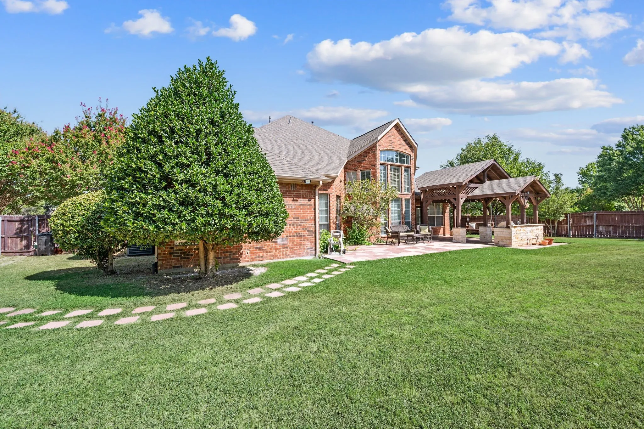Expansive rear yard featuring a large patio, stone paver walkway, and mature landscaping