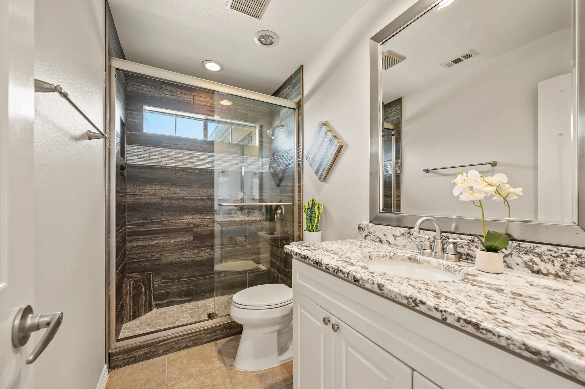 Glass-enclosed shower with wood-finish tile surround, white vanity with a granite countertop, and a recessed ceiling light