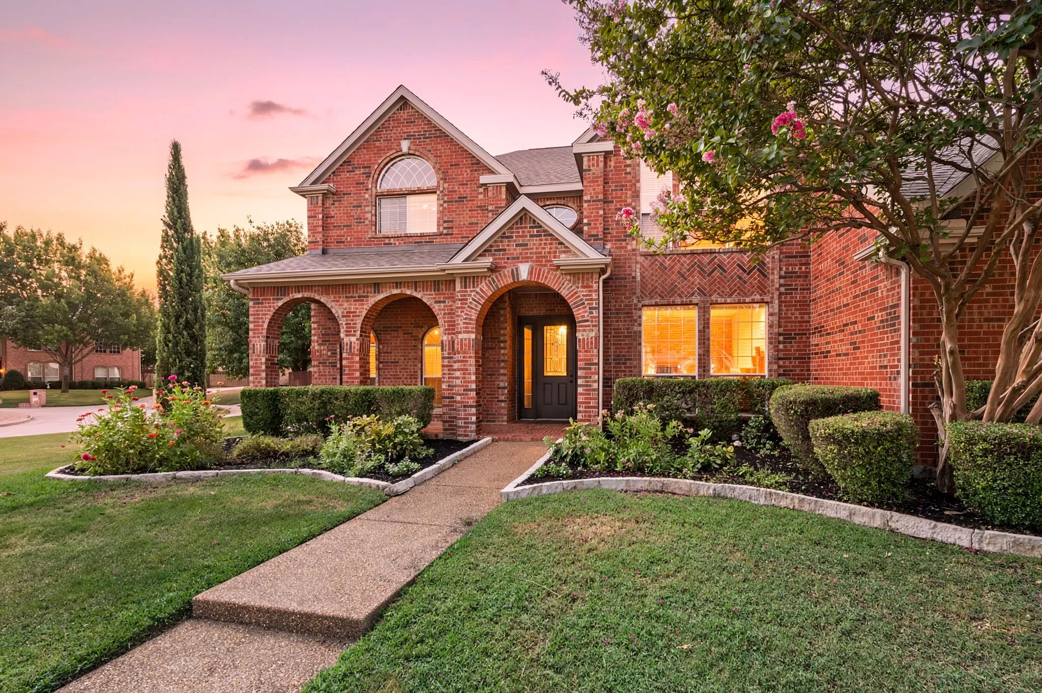 Brick exterior featuring arched entryway, decorative landscaping, paved walkway, and transom window