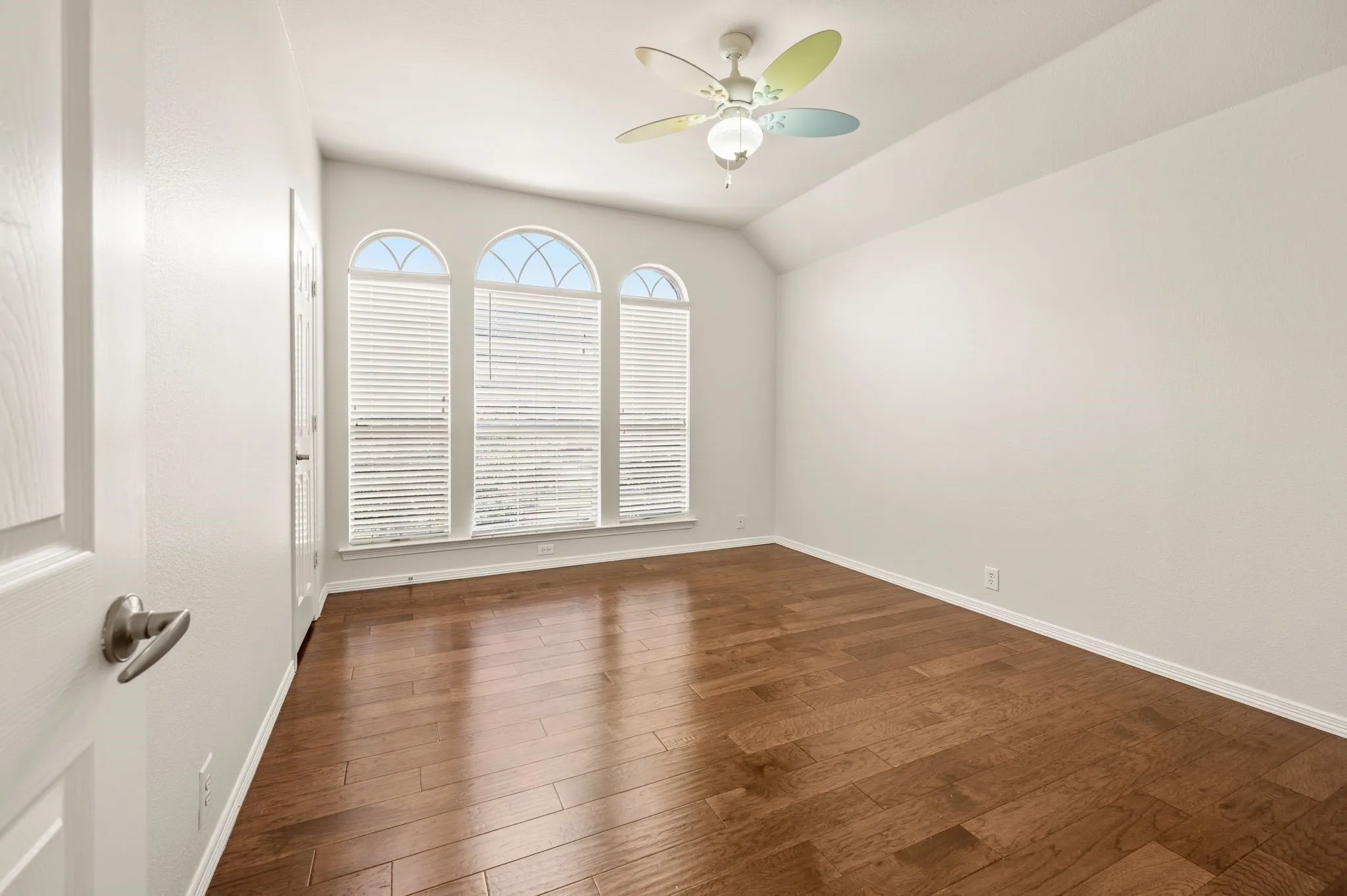 Vaulted ceiling, wood-finish flooring, arched windows with blinds, recessed lighting, and a ceiling fan
