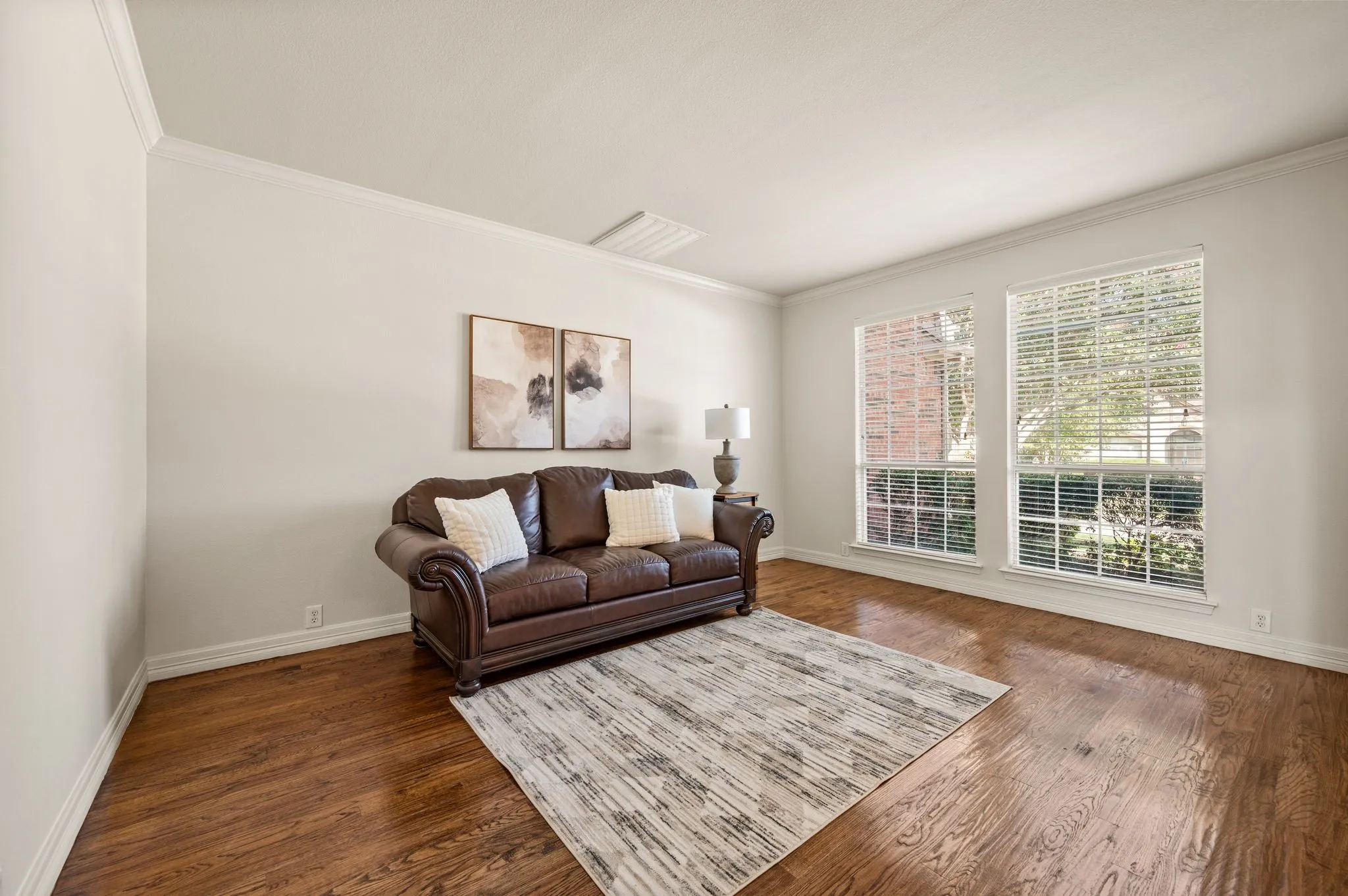 Hardwood flooring, crown molding, two large windows with blinds, and white painted walls