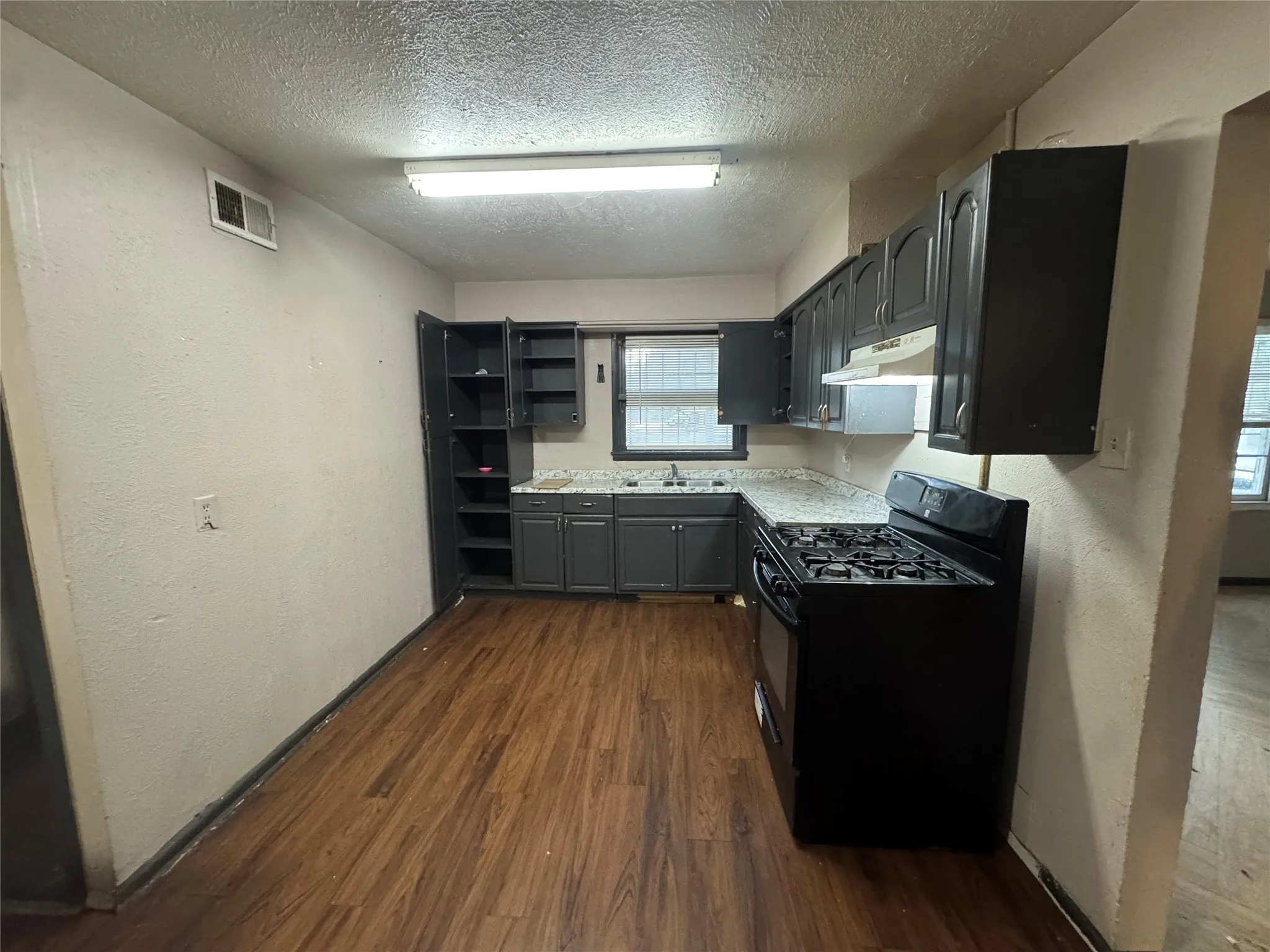 Kitchen featuring wood-finish flooring, dark cabinetry, light-toned countertops, and a built-in range