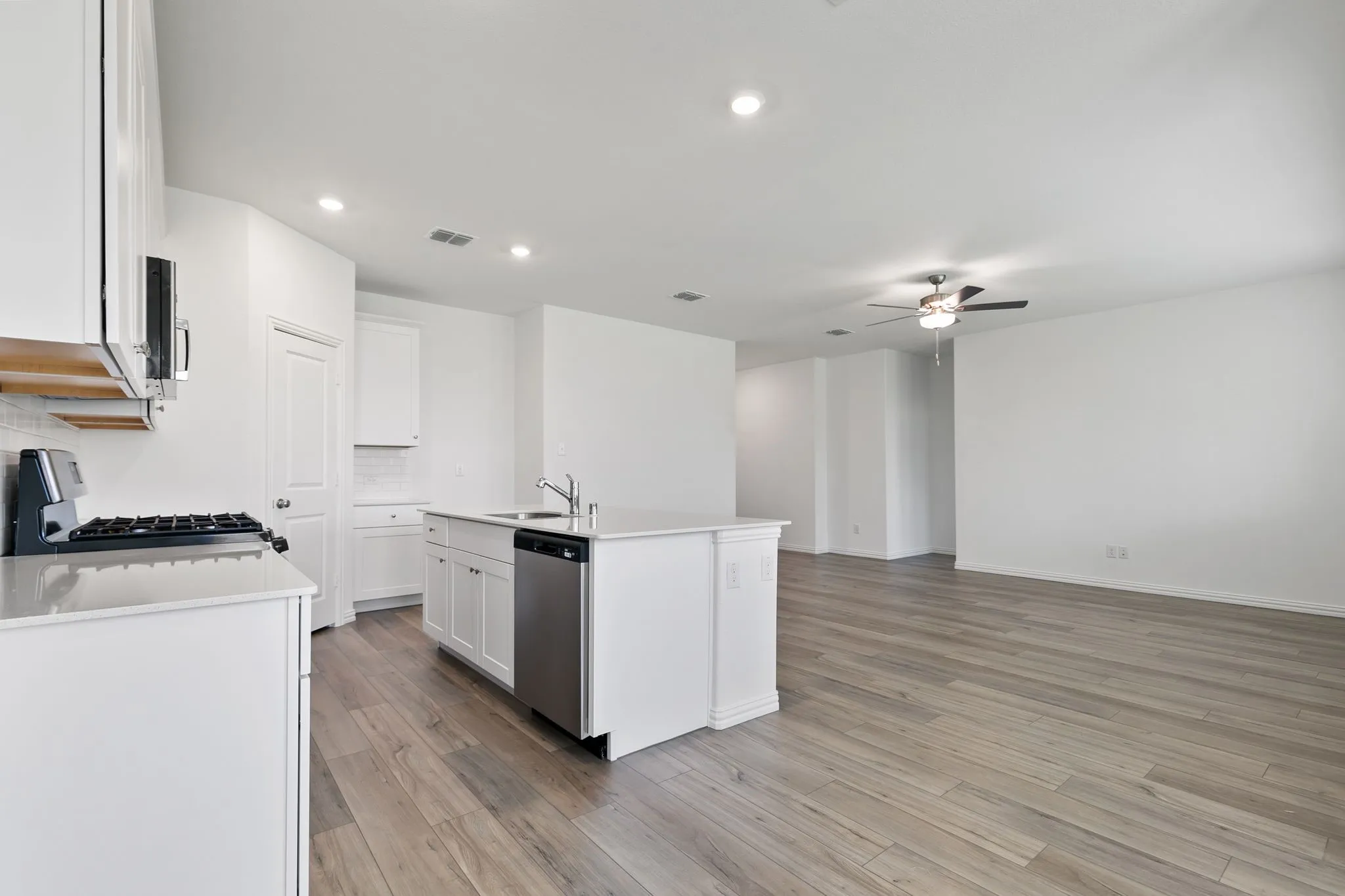 Kitchen featuring gas stove, a kitchen island with sink, white cabinets, light wood-type flooring, and dishwasher