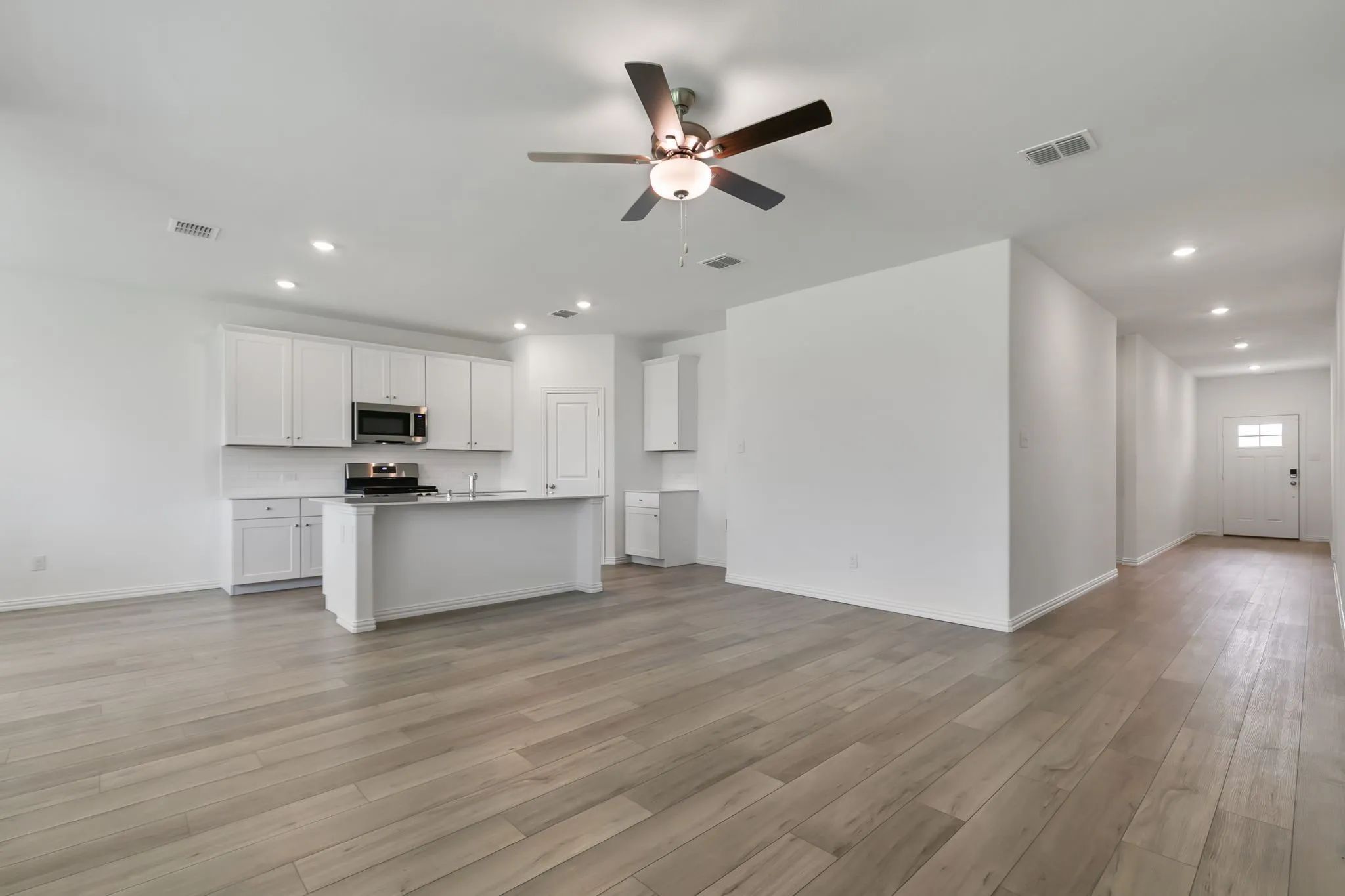 Kitchen with appliances with stainless steel finishes, ceiling fan, light wood-type flooring, white cabinetry, and a kitchen island with sink