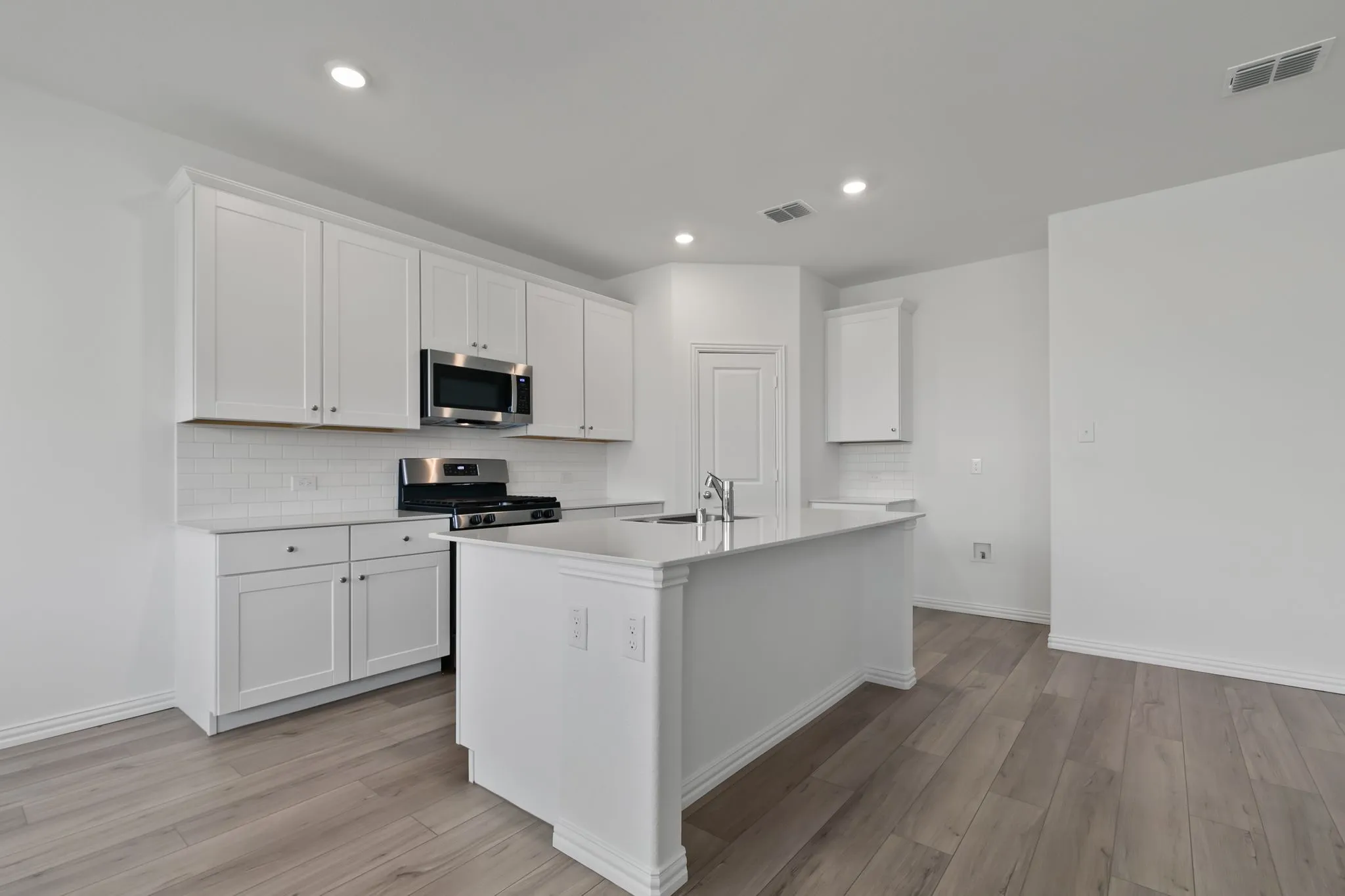 Kitchen with a kitchen island with sink, stainless steel appliances, light hardwood / wood-style floors, and white cabinetry