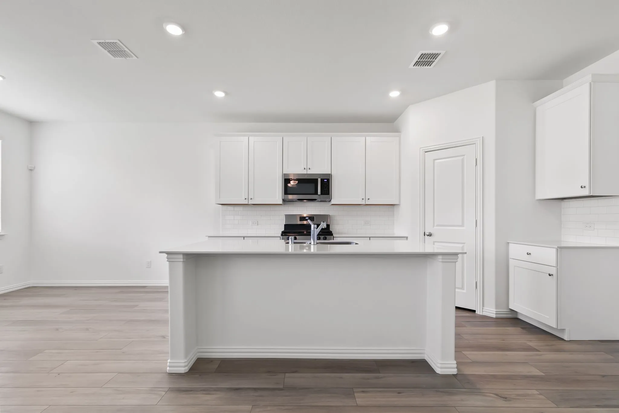 Kitchen with white cabinets, backsplash, stainless steel appliances, a center island with sink, and light hardwood / wood-style floors