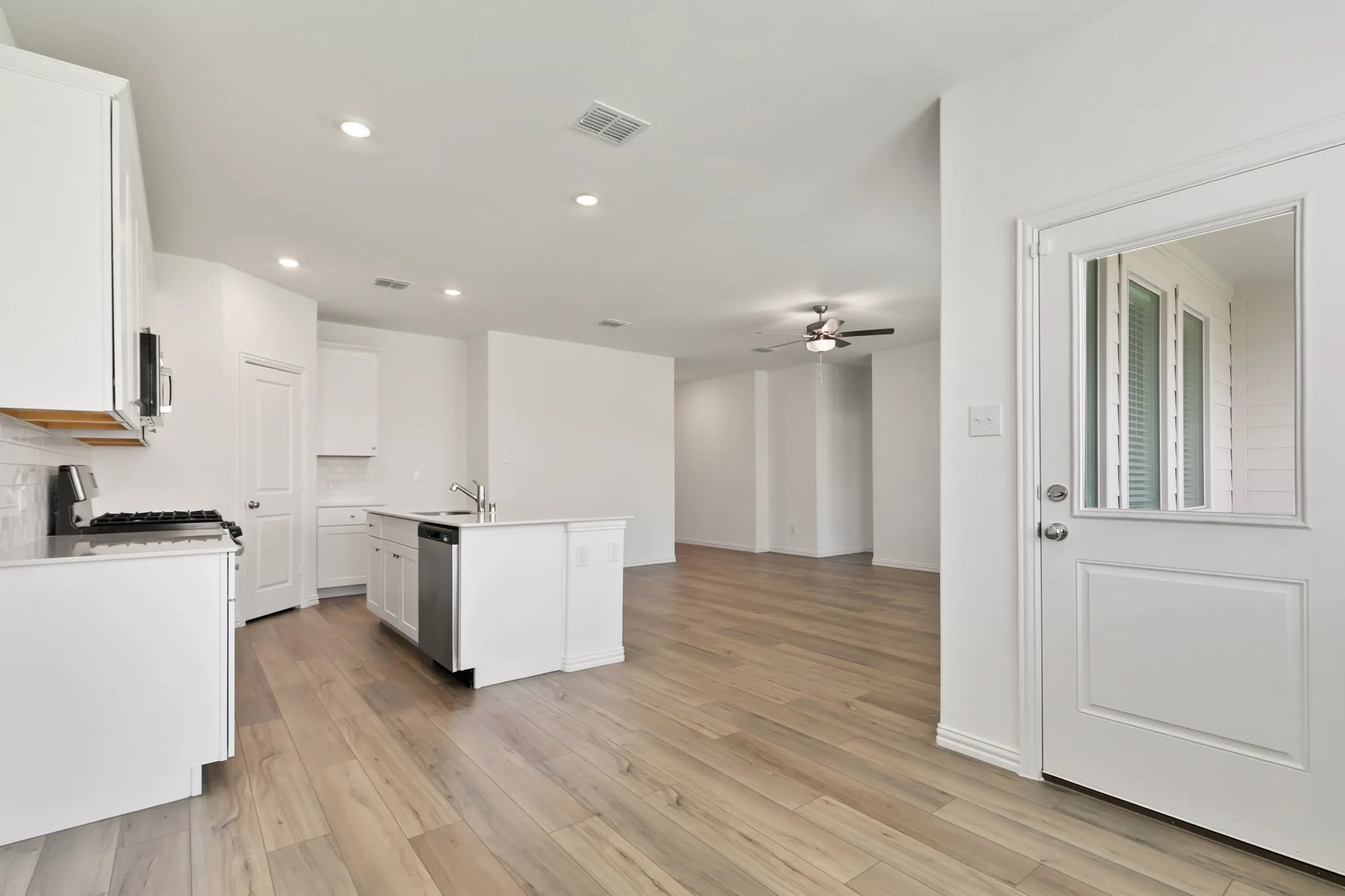 Kitchen with tasteful backsplash, light hardwood / wood-style flooring, ceiling fan, and a center island with sink