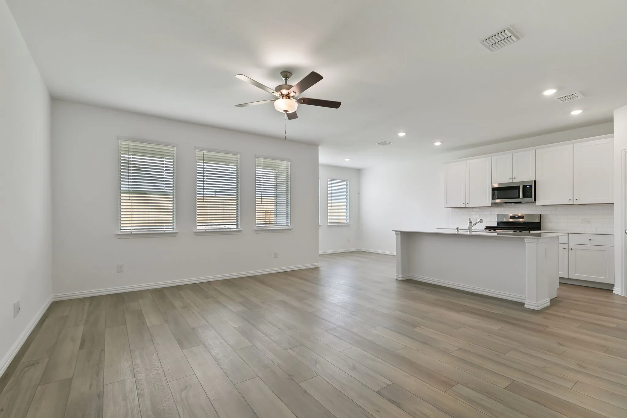Kitchen featuring backsplash, appliances with stainless steel finishes, white cabinetry, and a center island with sink