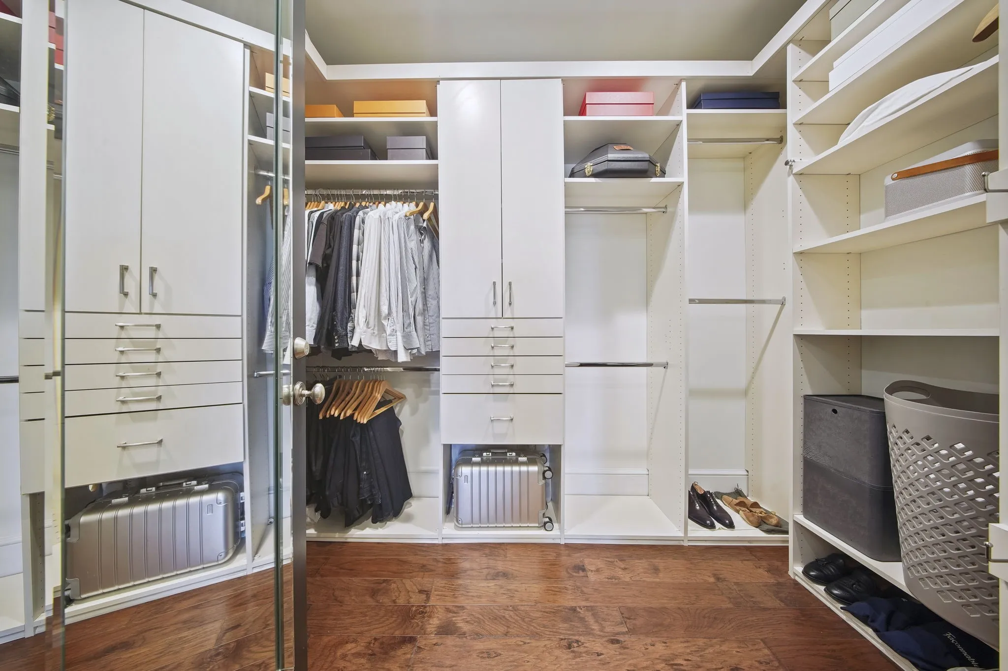 Luxurious walk-in closet featuring custom white cabinetry with abundant drawer storage, built-in shelving throughout, a dedicated clothing rod with multiple hanging sections, recessed lighting, and wood-finish flooring