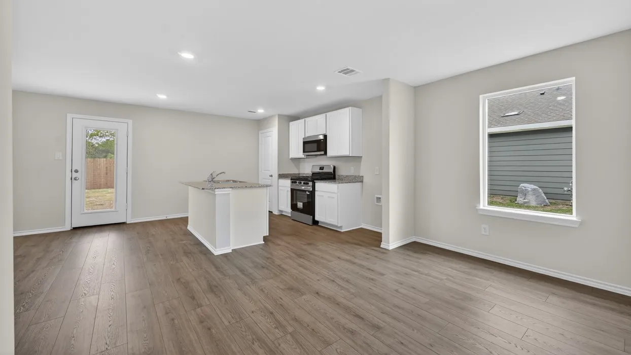 Open-concept living area with wood-finish flooring, white cabinetry, stainless steel appliances, a kitchen island with a sink, and a glass-paned exterior door
