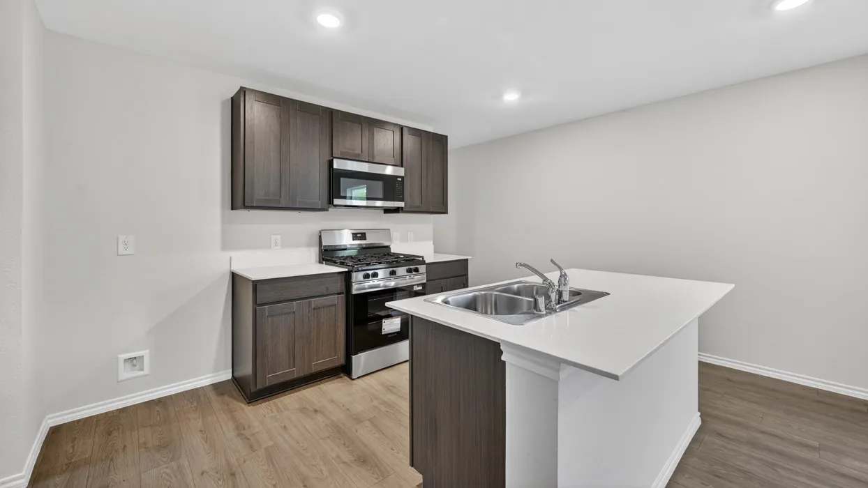 Kitchen featuring wood-finish flooring, dark wood-finish cabinetry, white countertops, stainless steel appliances, and a kitchen island with an integrated double sink