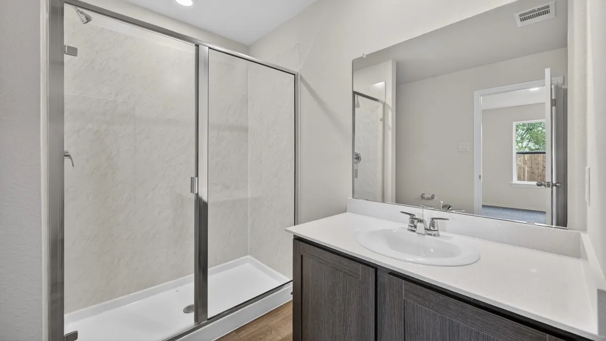 Walk-in shower with sliding glass door, single vanity with integrated sink, quartz-finish countertop, and wood-finish cabinetry