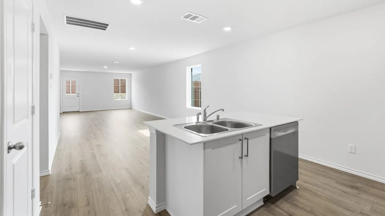 Open-concept living space featuring wood-finish flooring, recessed lighting, and a kitchen island with a double basin sink, stainless steel faucet, and integrated dishwasher