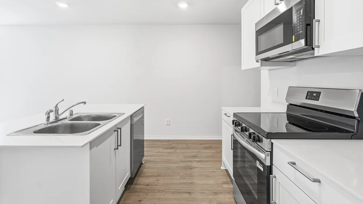 Kitchen featuring white cabinetry, stainless steel appliances, wood-finish flooring, white countertops, and a double basin sink