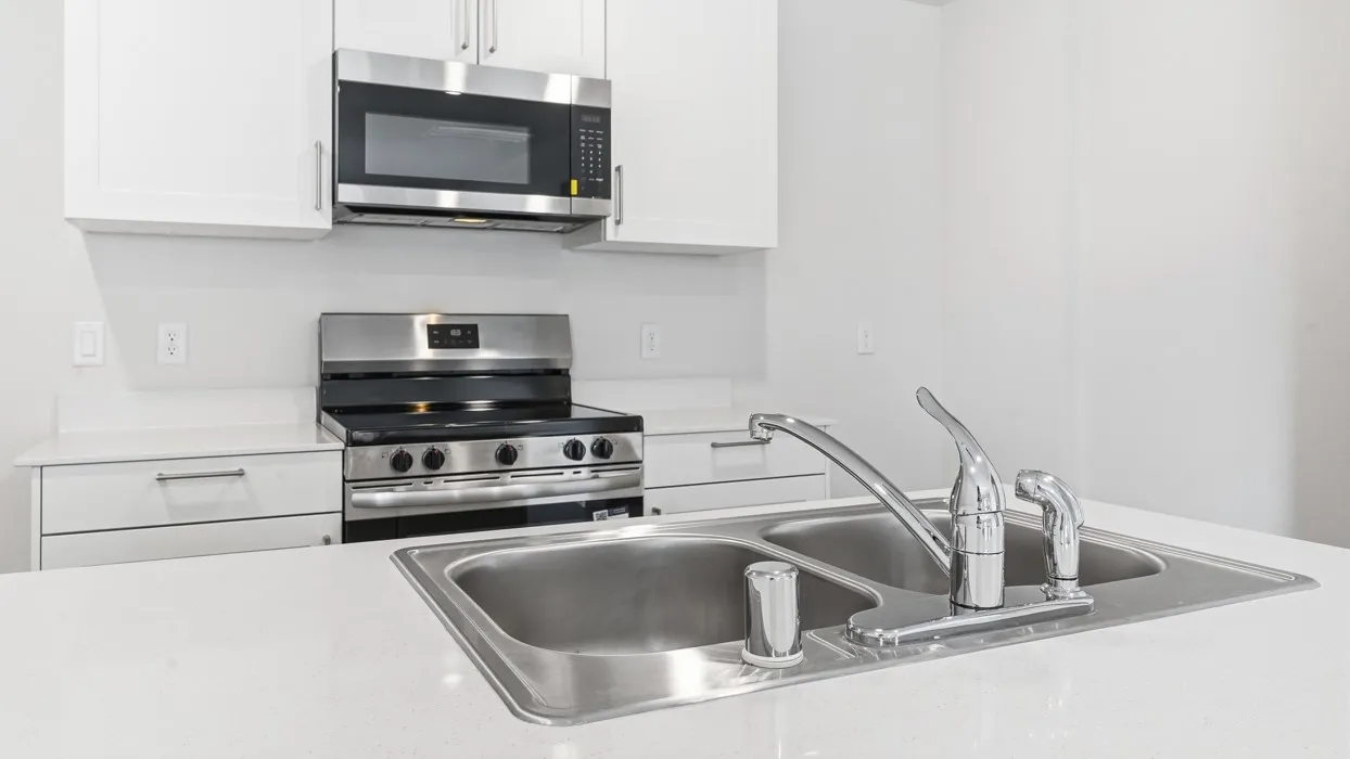 Kitchen featuring white cabinetry, stainless steel appliances including an oven range and microwave, light-toned countertops, and a double basin sink with a chrome faucet