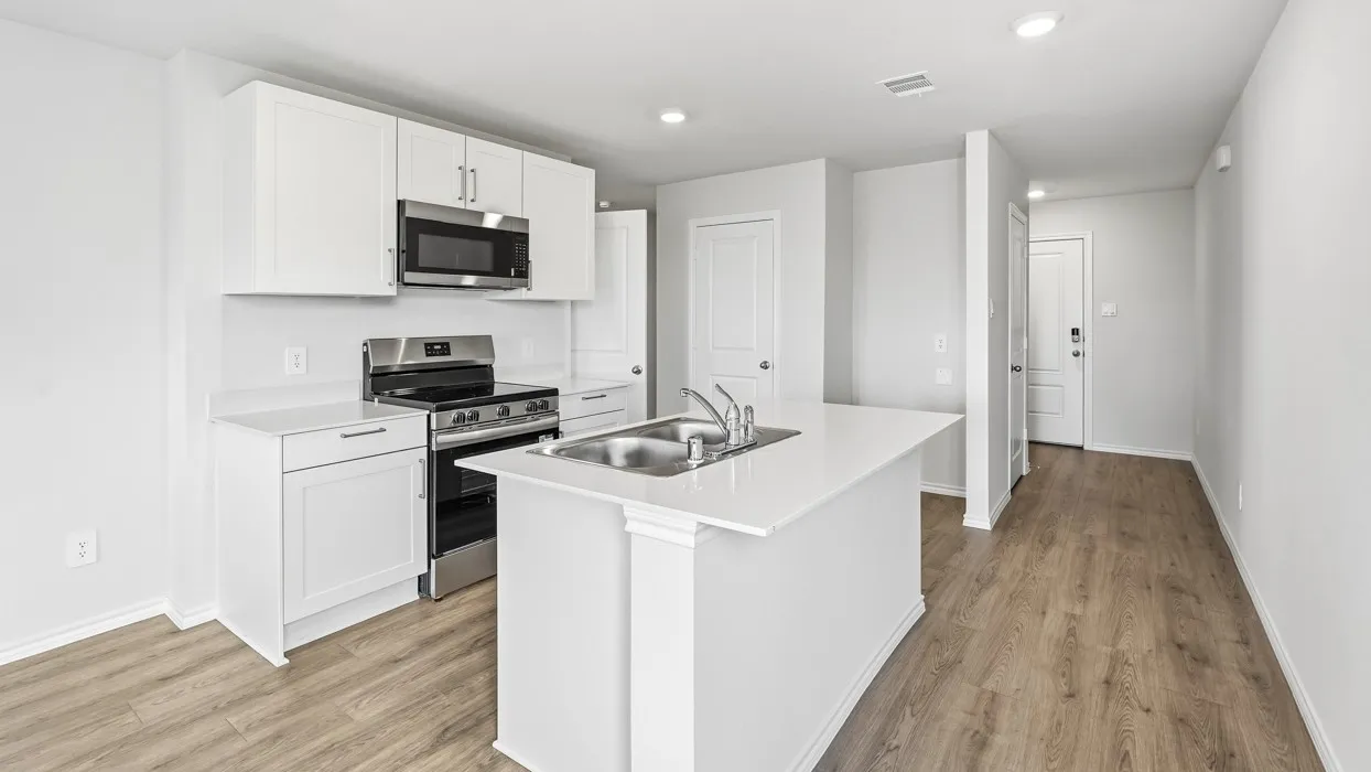 Kitchen featuring white cabinetry, stainless steel appliances, a kitchen island with an integrated sink, white countertops, and wood-finish flooring