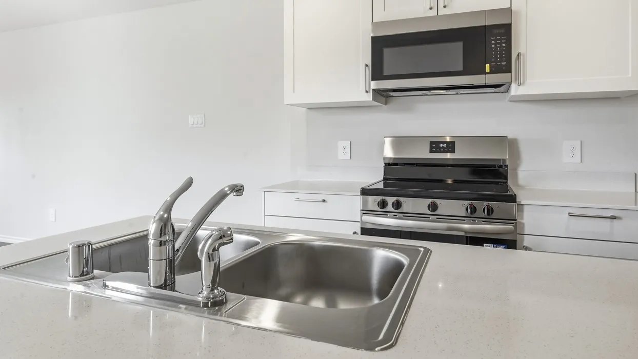Stainless steel double basin sink with chrome faucet, white cabinetry, integrated stainless steel microwave, and stainless steel range