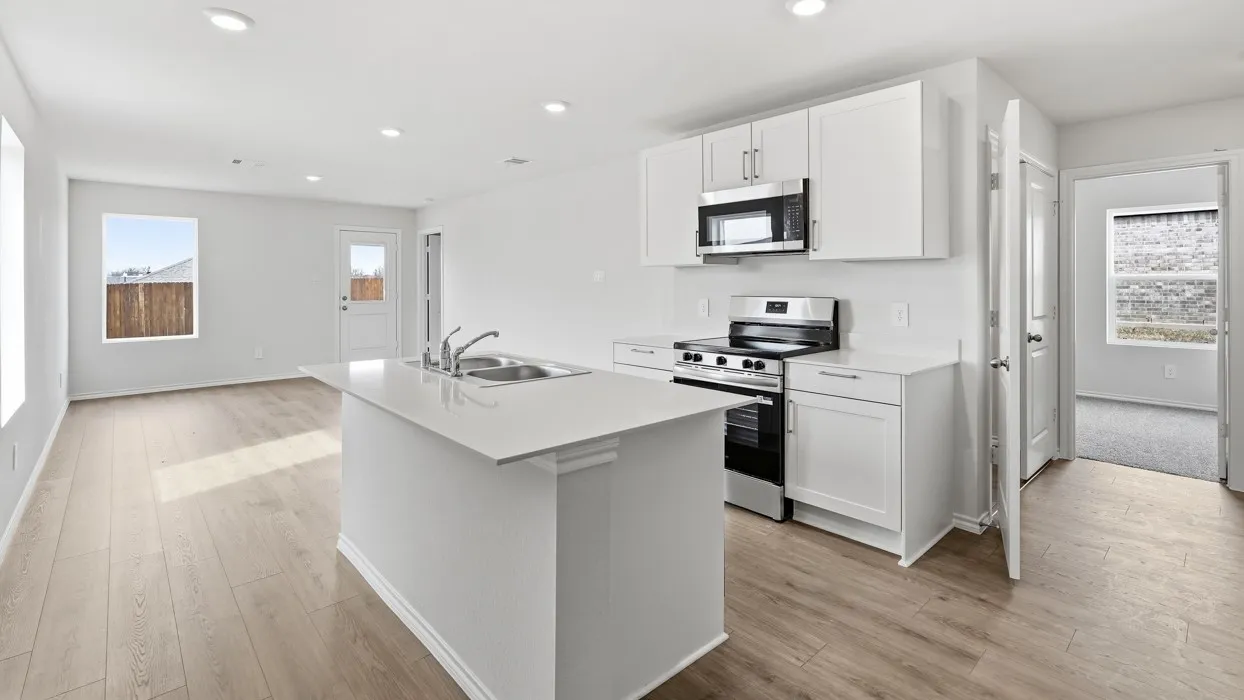Kitchen island with an undermount dual-basin sink, stainless steel appliances, white cabinetry, and wood-finish flooring throughout