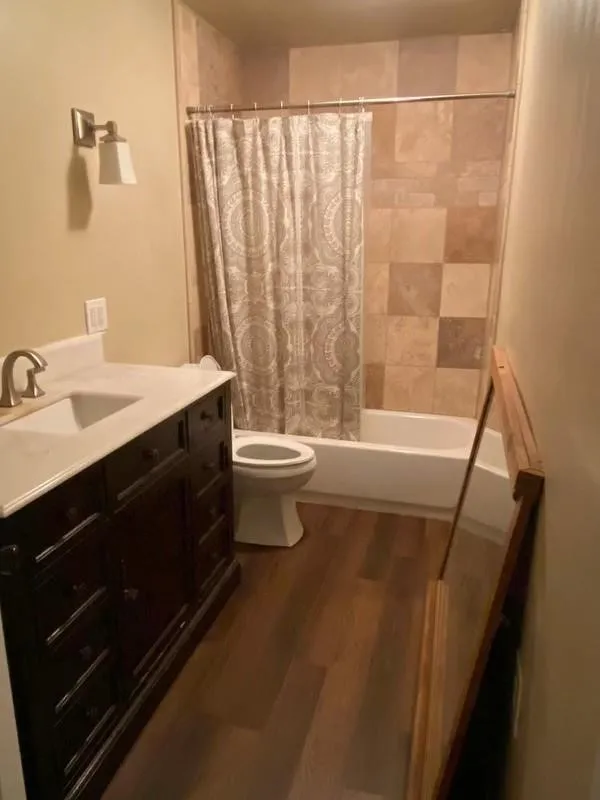 Wood-finish flooring with a dark wood vanity, white countertop, and integrated sink