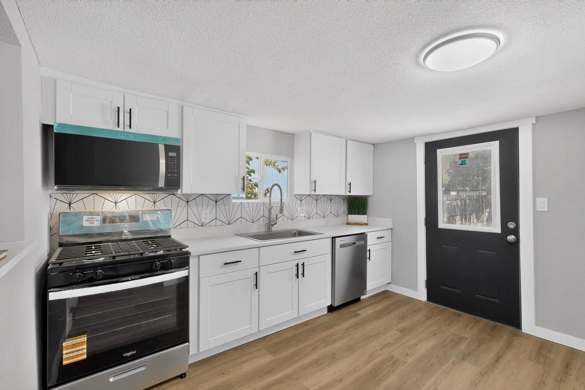 Kitchen featuring white shaker cabinetry, white countertops, stainless steel appliances, wood-finish flooring, and a geometric tile backsplash