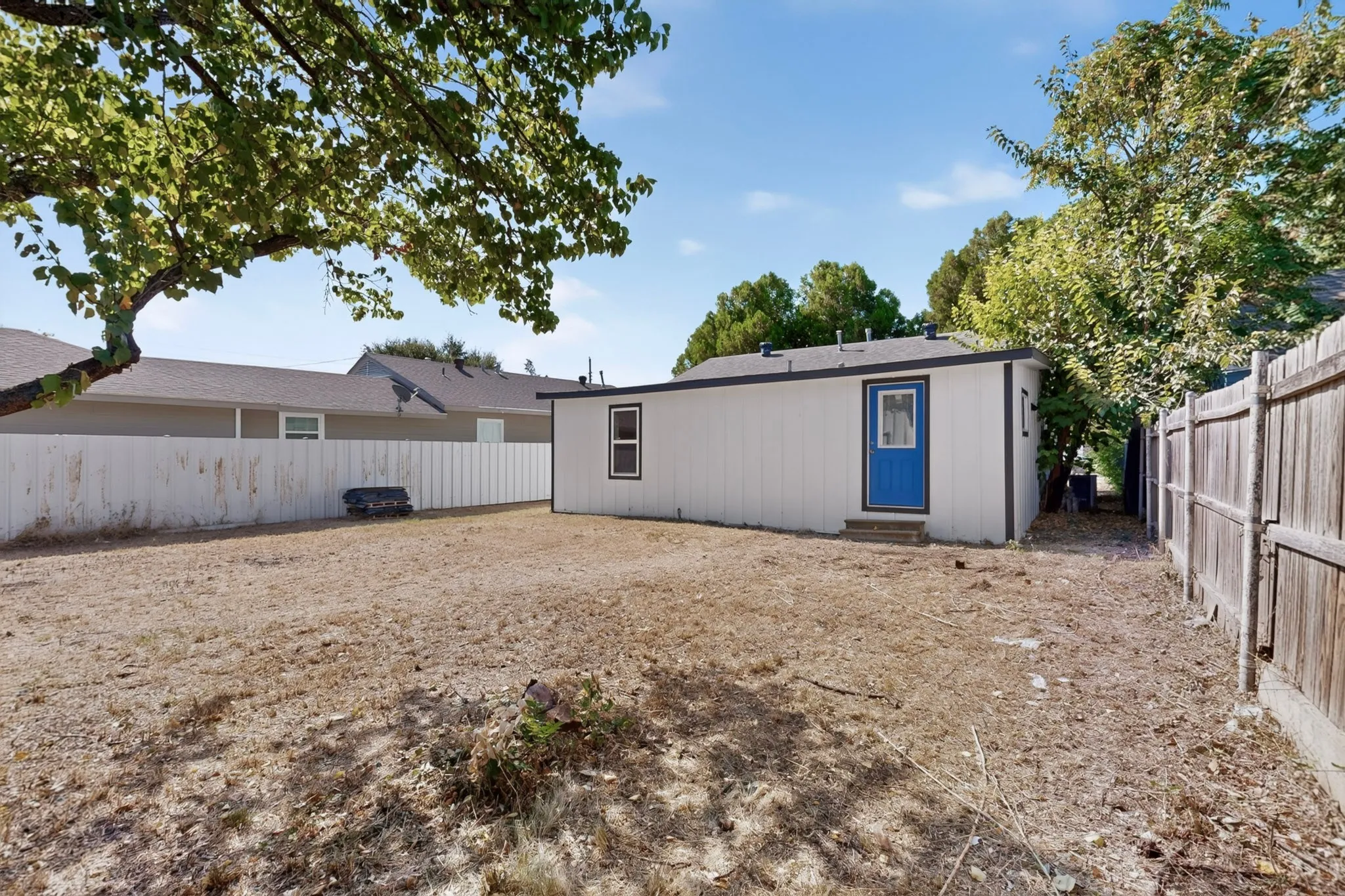 Spacious backyard with mature shade trees and level grounds, bordered by wood-finish fencing