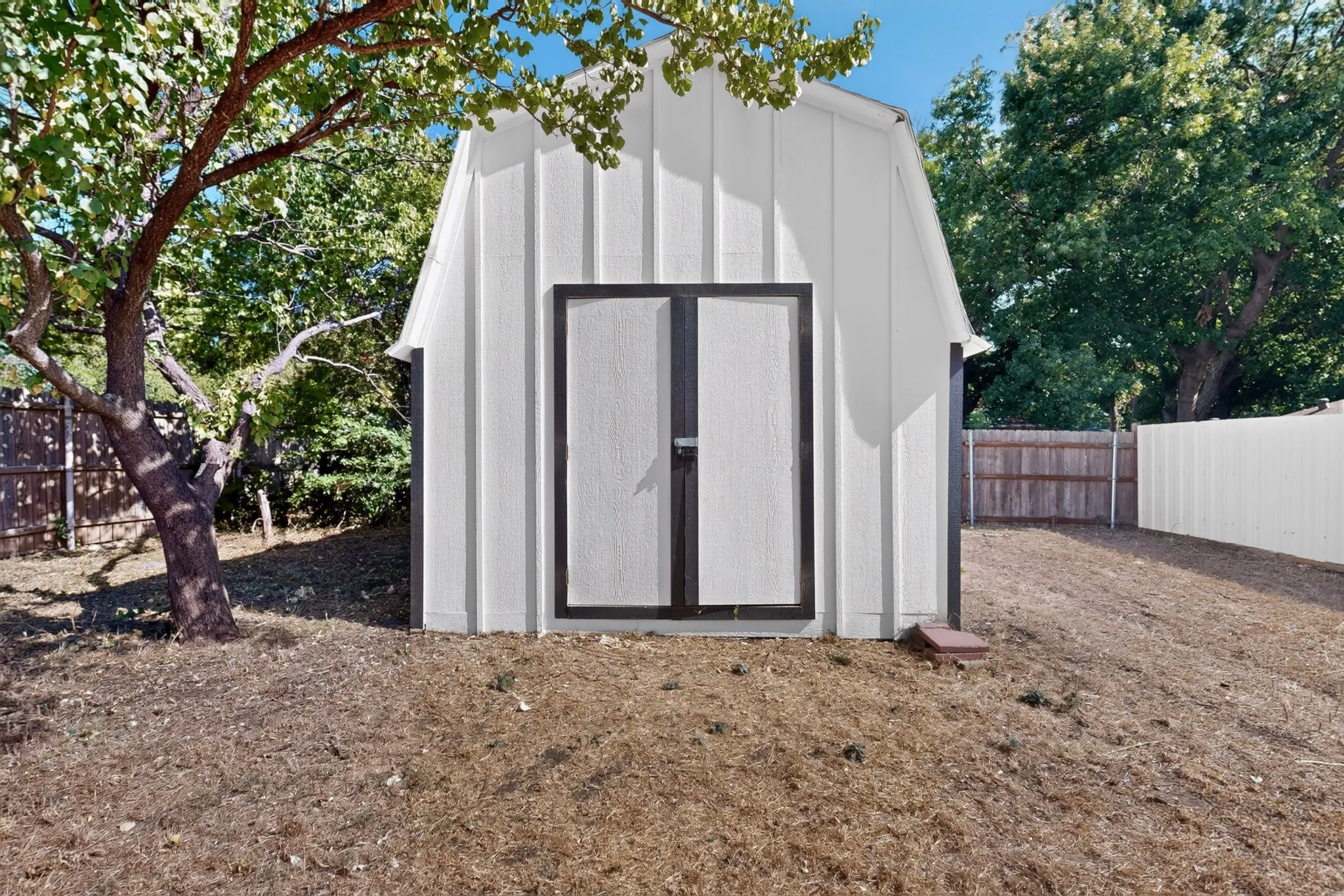 White board-and-batten outbuilding featuring dark trim and double doors