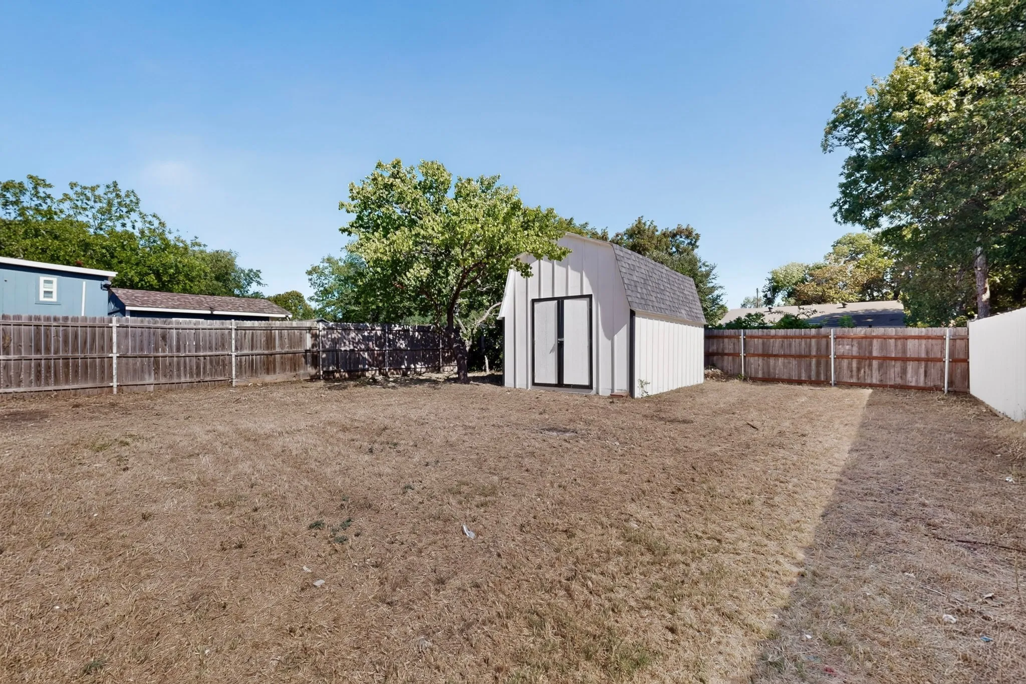Spacious yard featuring a detached storage shed with double doors, wood fencing, and mature trees