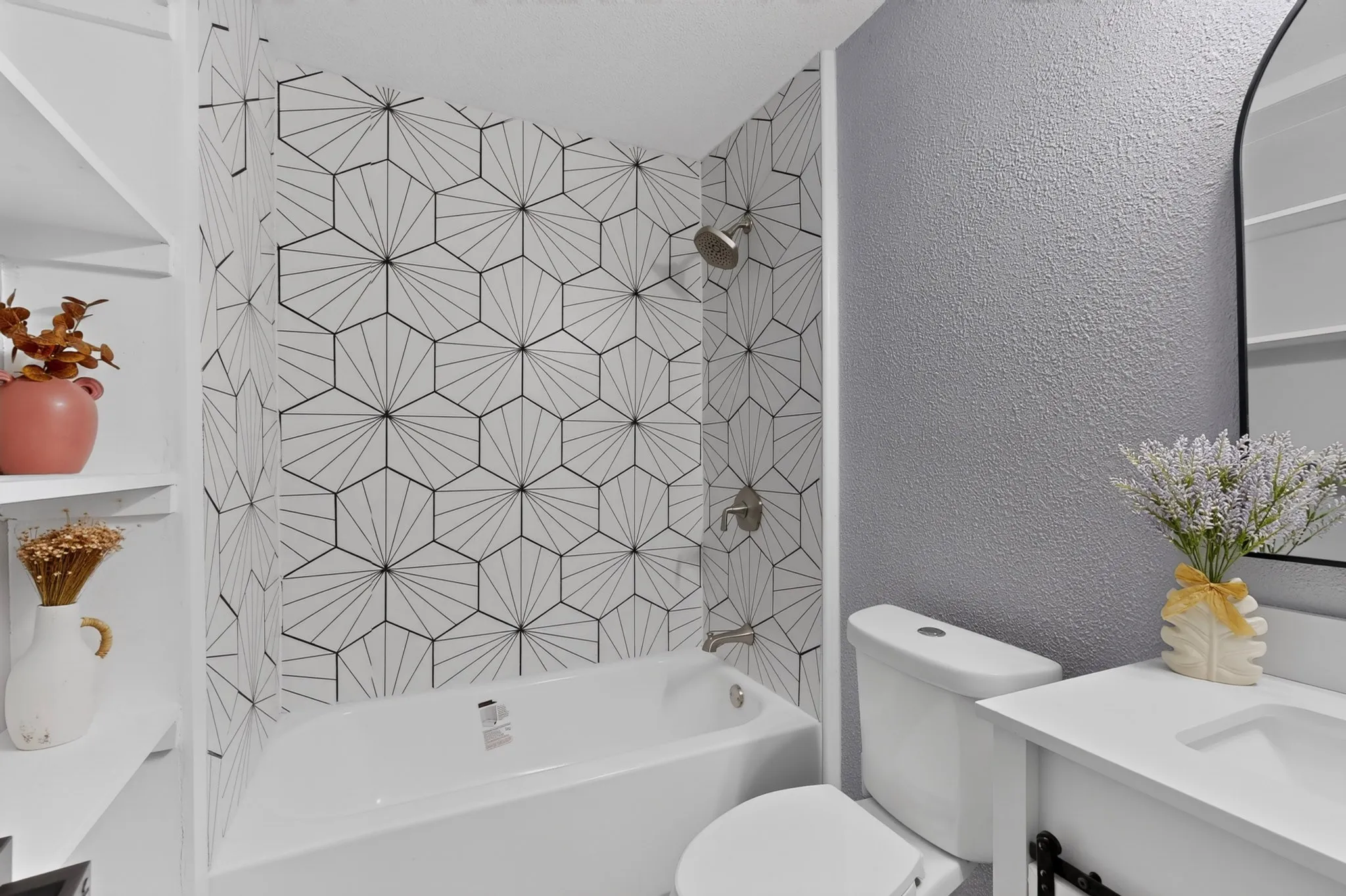 White bathtub with geometric-patterned tile surround, brushed nickel shower fixtures, and white built-in shelving