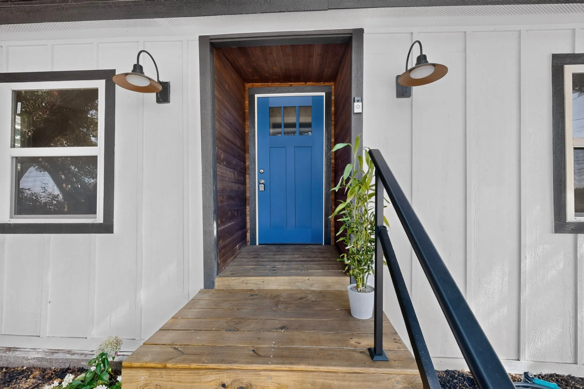 Vertical white exterior siding, wood-finish entry, vibrant blue entry door, and black exterior wall sconces