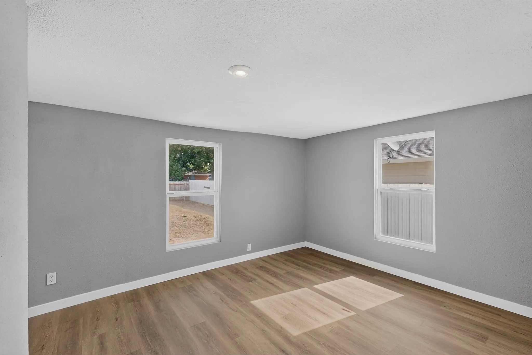 Spacious room featuring wood-finish flooring, two windows, recessed lighting, and neutral wall paint