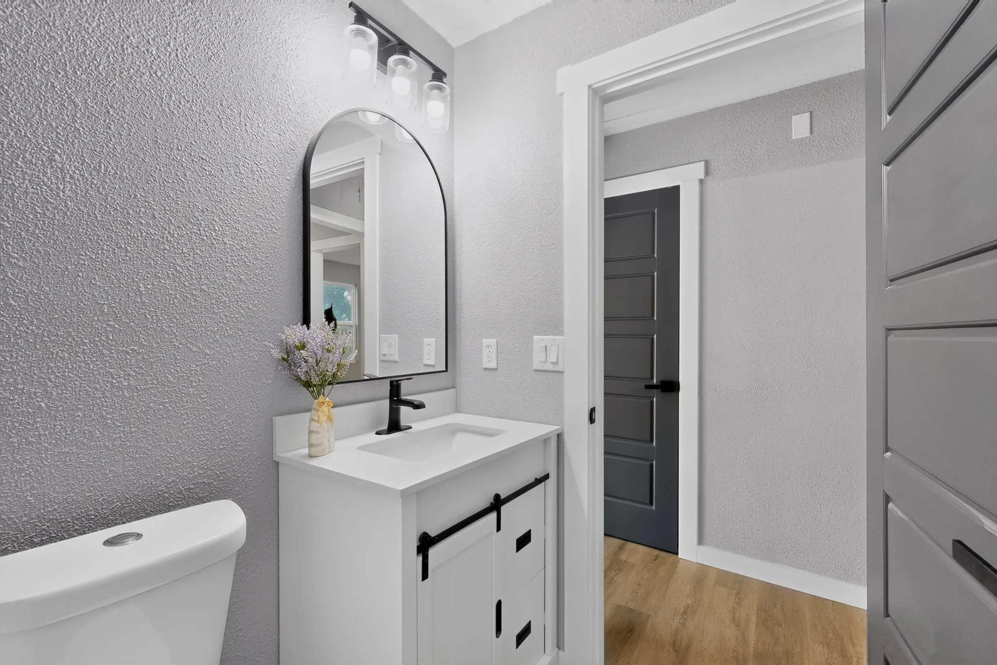 White vanity with a single basin sink, matte black faucet, and arched mirror