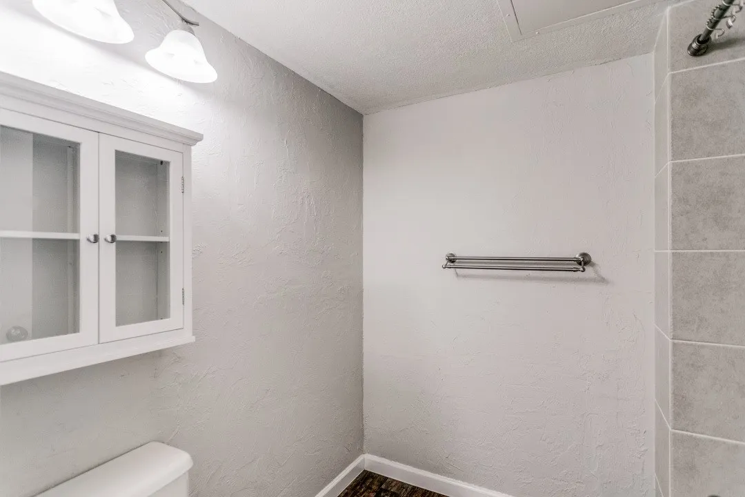 White wall-mounted cabinet with glass-front doors, dual light fixture, and chrome towel bar