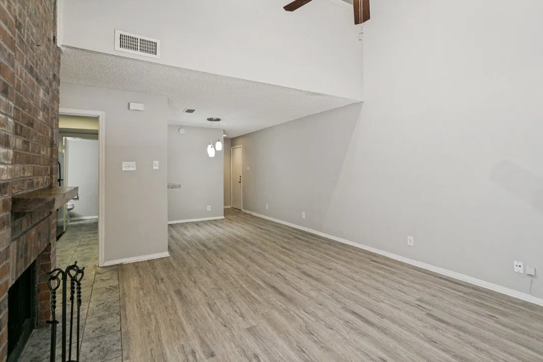 Spacious living area featuring wood-finish flooring, a brick fireplace with a mantle, and a vaulted ceiling with an exposed beam and ceiling fan