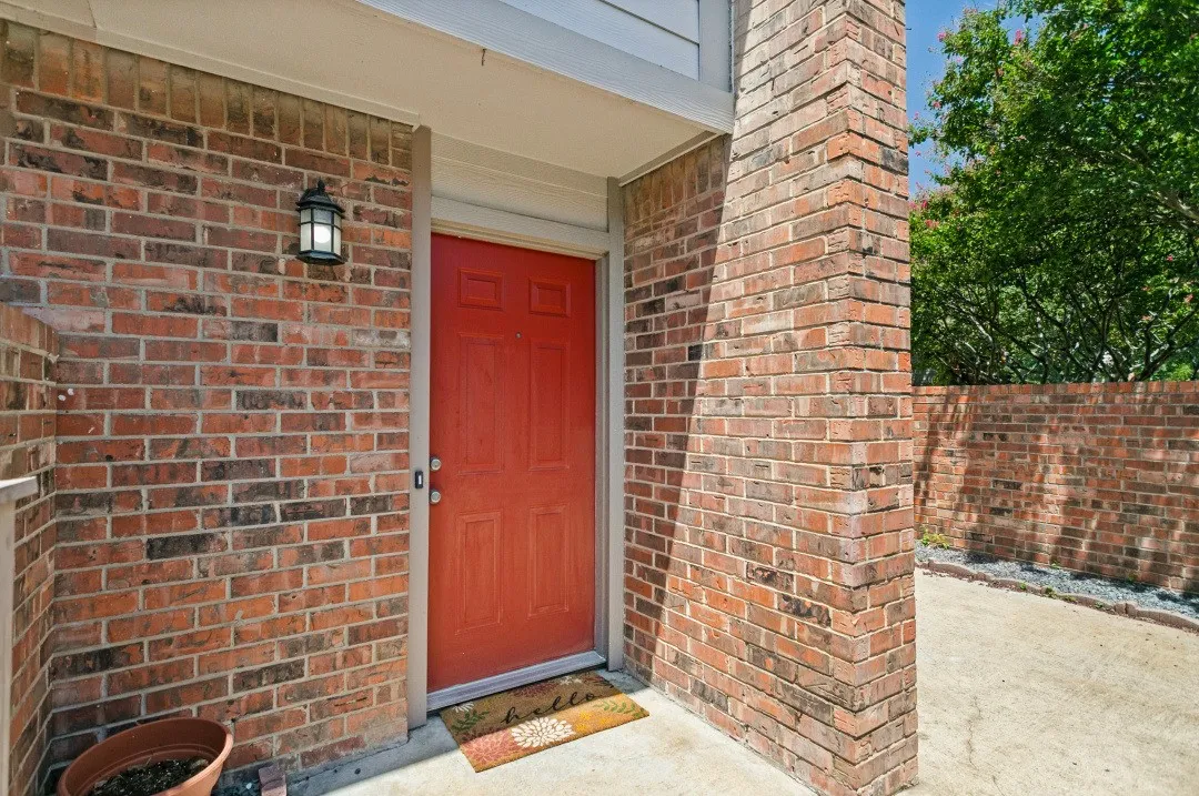 Brick exterior with a red paneled entry door, covered porch, and exterior wall lantern