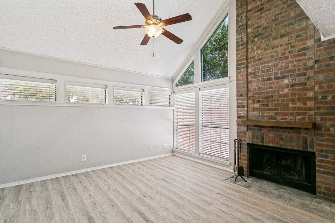 Vaulted ceiling with a ceiling fan, brick fireplace with wood mantel, wood-finish flooring, and multiple windows