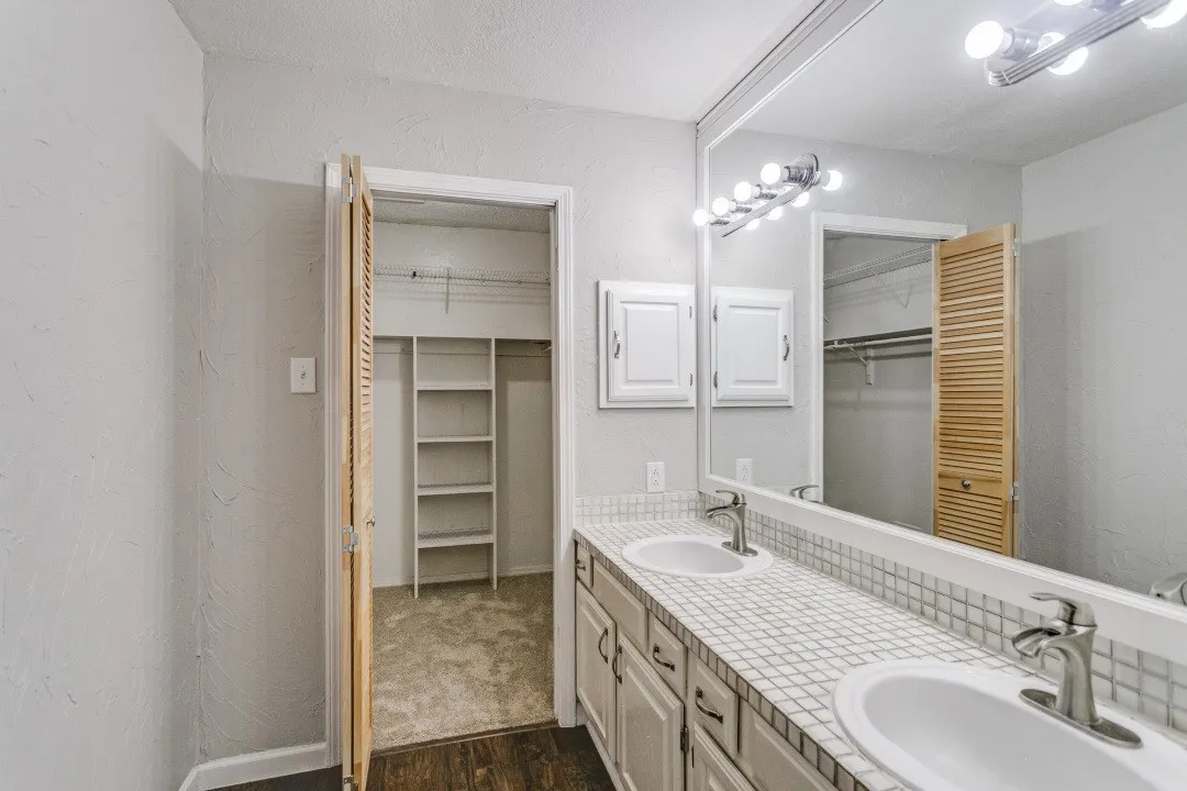 Dual vanity with white tile countertop and integrated sinks, wall-mounted mirror, and overhead vanity lighting