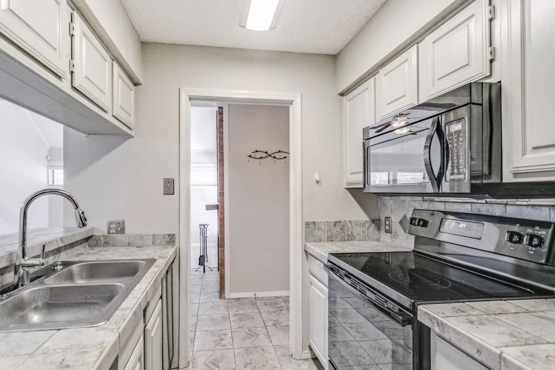 Kitchen featuring white cabinetry, tile countertops, a double basin stainless steel sink, and a black range with an overhead microwave