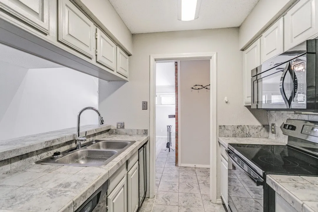 Galley-style kitchen featuring white cabinetry, stone-look countertops, stainless steel appliances including a built-in microwave and range, tile flooring, and a prep sink with gooseneck faucet