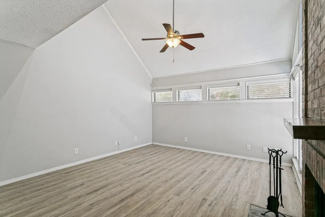 Vaulted ceiling with a ceiling fan, wood-finish flooring, brick-faced fireplace, and upper transom windows