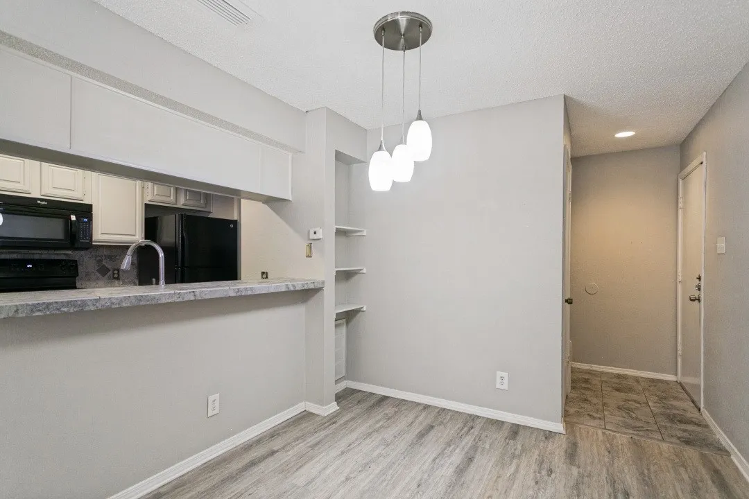 Wood-finish flooring, kitchen pass-through with stone-look countertop, white upper and lower cabinetry, built-in shelving, and a three-light pendant fixture
