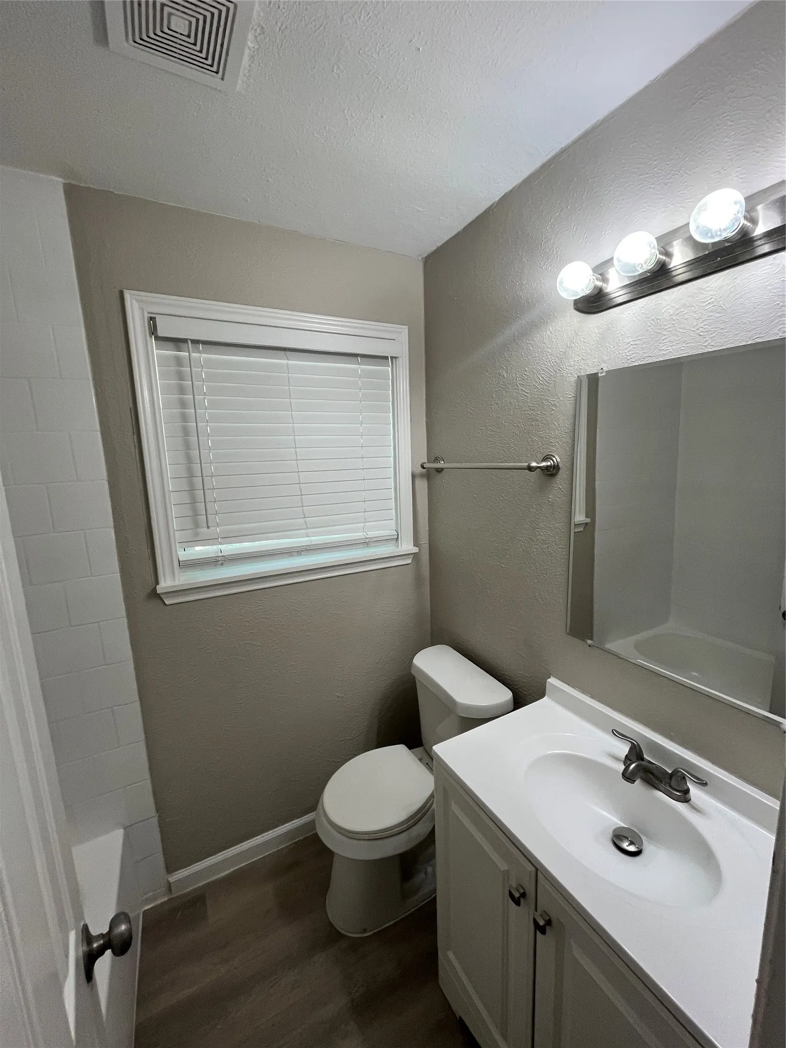 Bathroom with wood-finish flooring, white vanity with integrated sink, chrome-finish faucet, and coordinating mirror