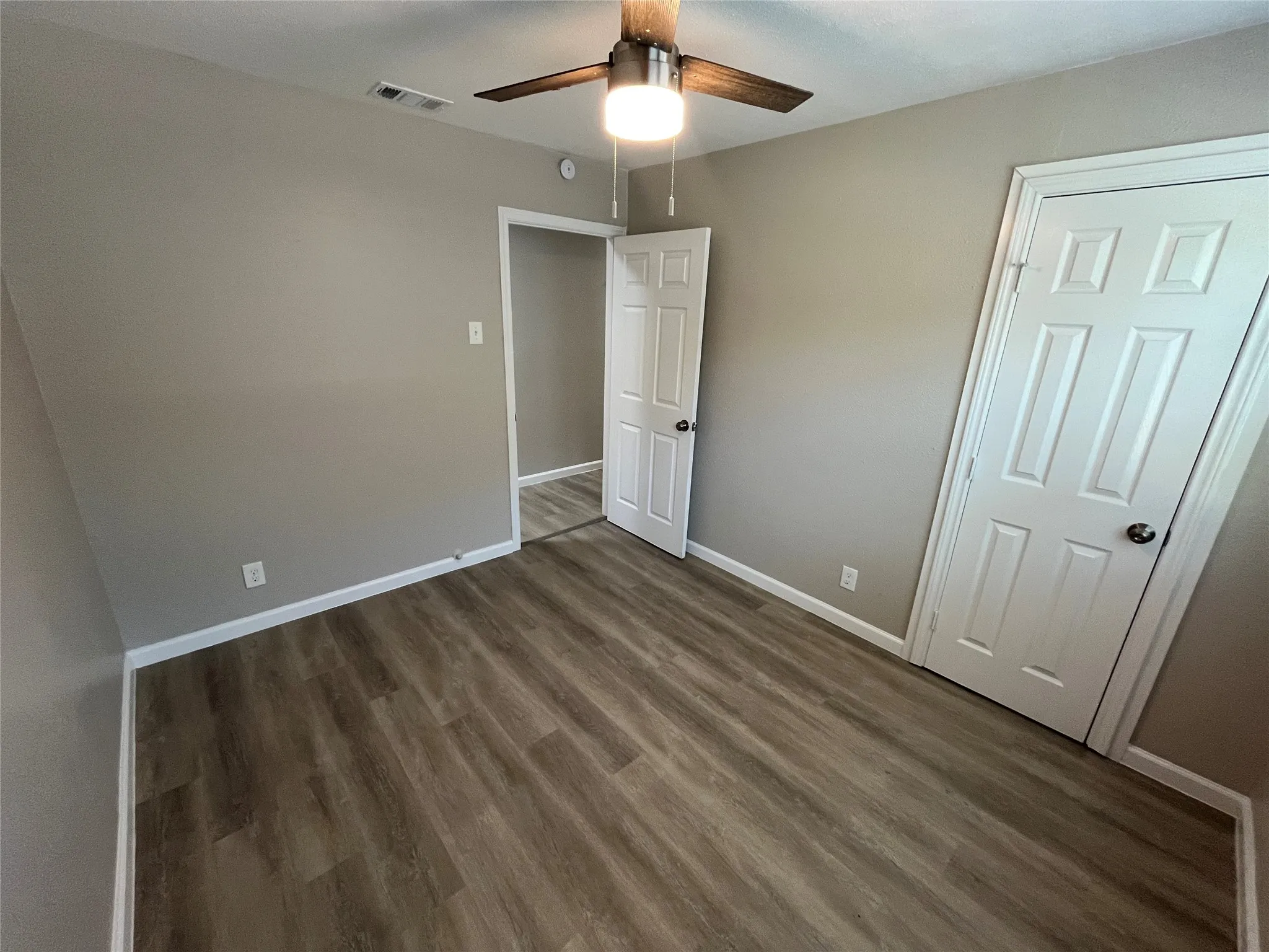 Wood-finish flooring, neutral wall tones, white trim, ceiling fan with integrated lighting, and paneled doors