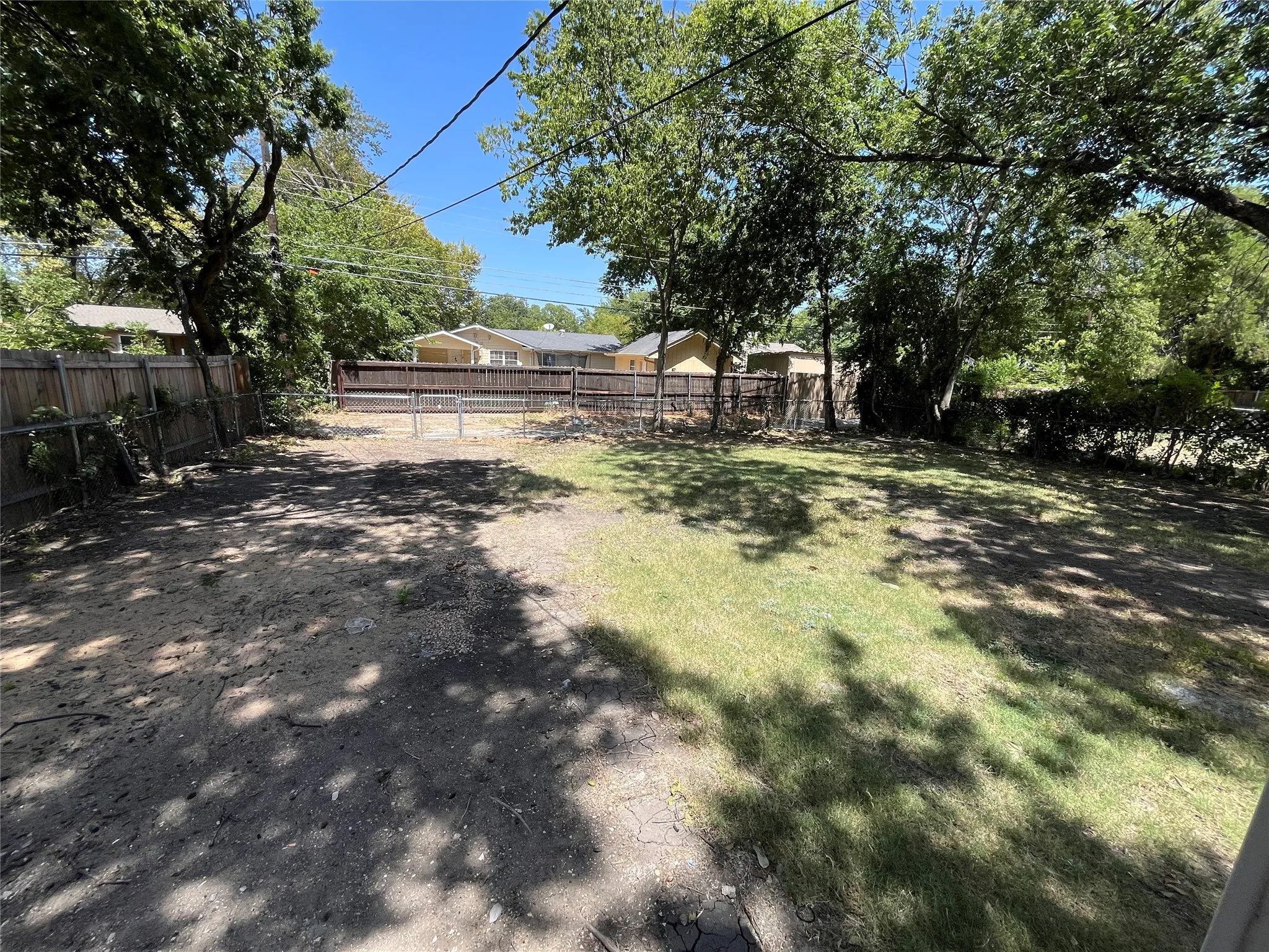 Expansive rear yard featuring mature trees, a wood privacy fence, and a chain-link gate