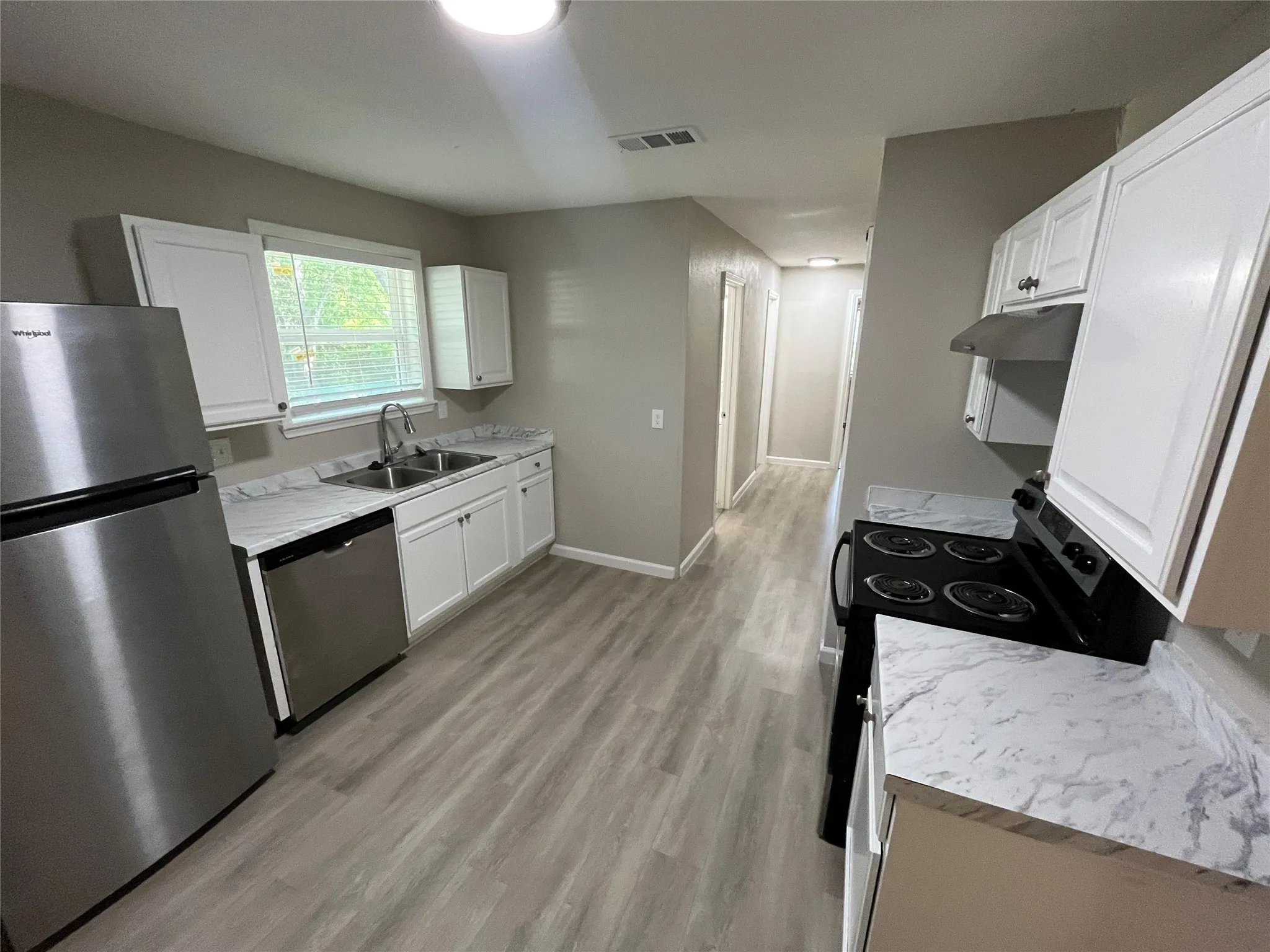 Kitchen featuring wood-finish flooring, white cabinetry, stainless steel appliances, and a double basin sink