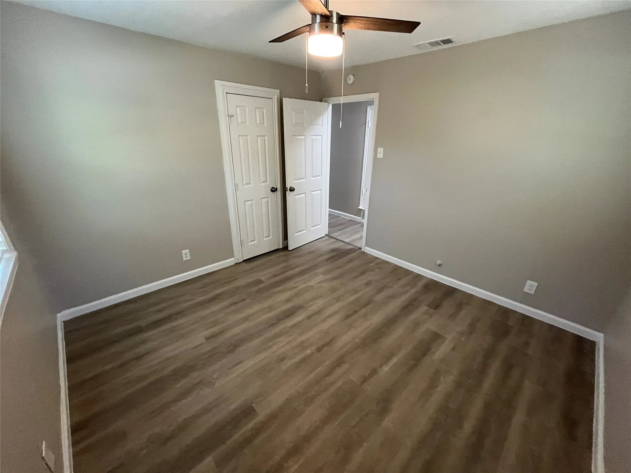 Wood-finish flooring, neutral wall paint, and a ceiling fan with integrated lighting