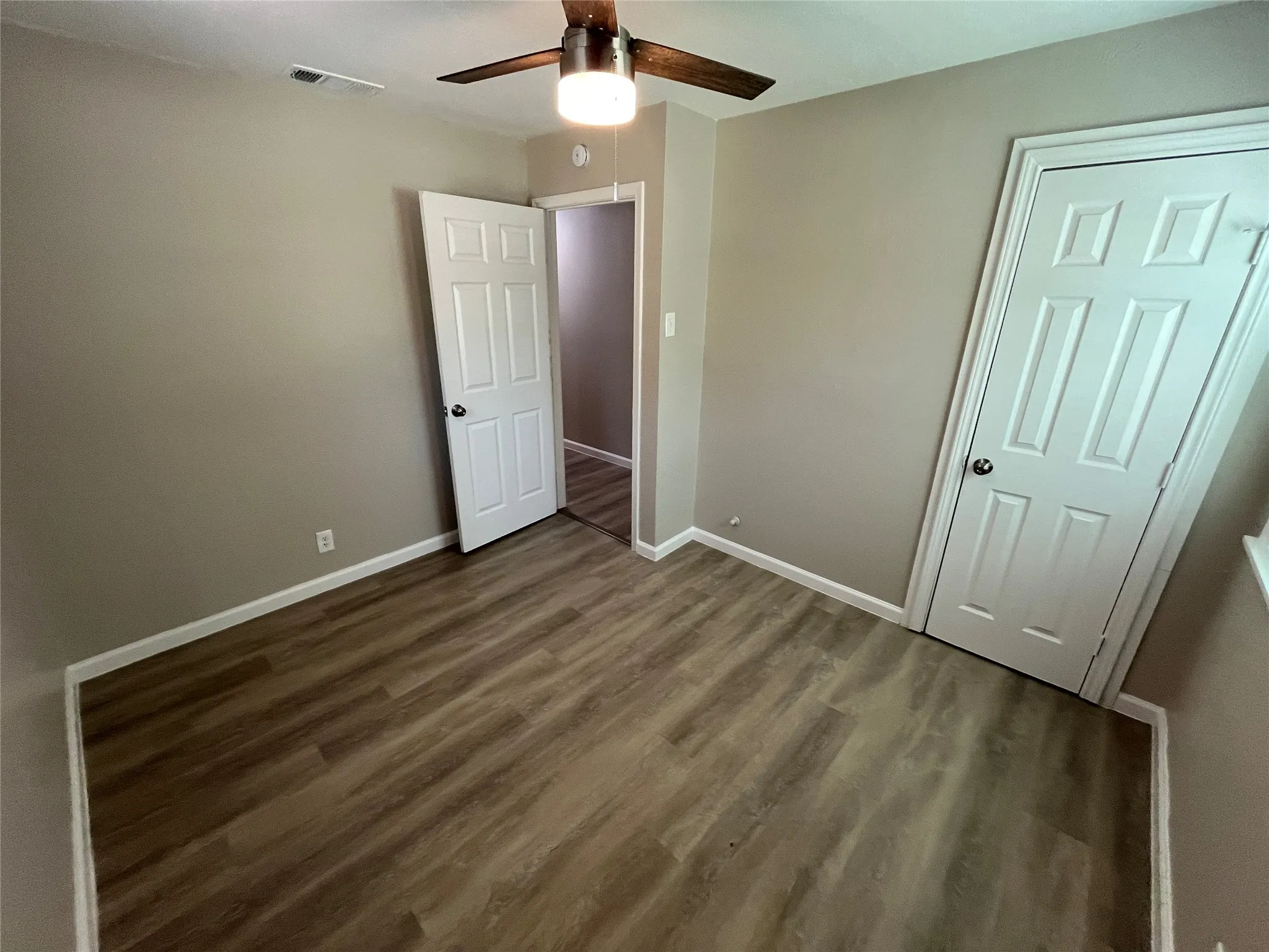 Wood-finish flooring, neutral wall paint, white trim, and a ceiling fan with light